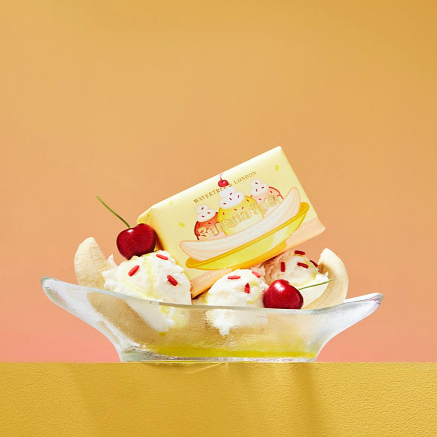 Dessert with banana, whipped cream, and cherry on a plate against a gradient background