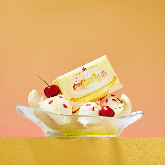 Dessert with banana, whipped cream, and cherry on a plate against a gradient background